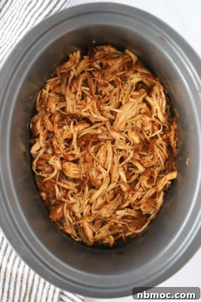 A slow cooker filled to the brim with perfectly cooked, shredded Slow Cooker BBQ Chicken, ready to be served. This showcases the ease and deliciousness of crockpot BBQ chicken recipes.