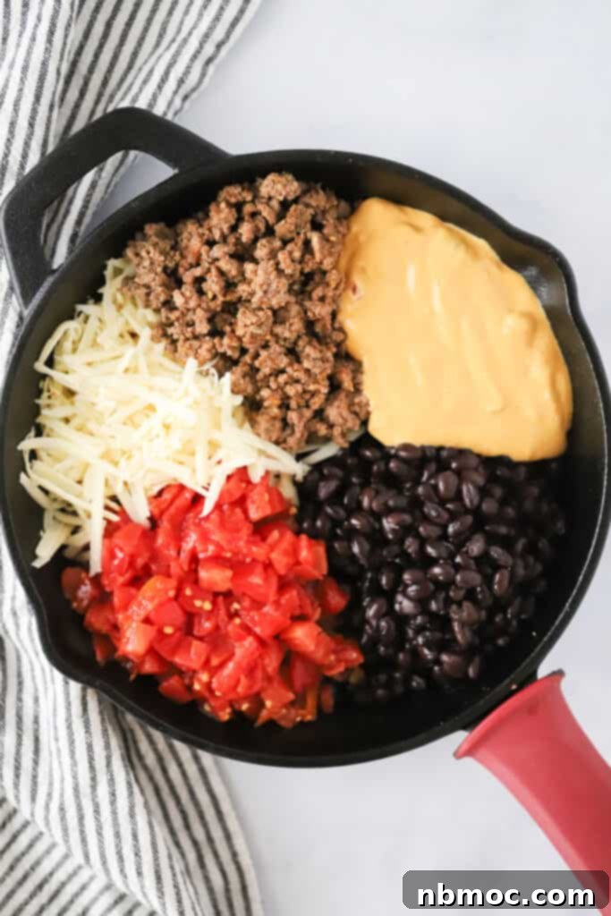 A cast iron skillet full of the ingredients to make this queso dip. baked queso dip with ground beef. Velveeta queso recipe, best cowboy queso.