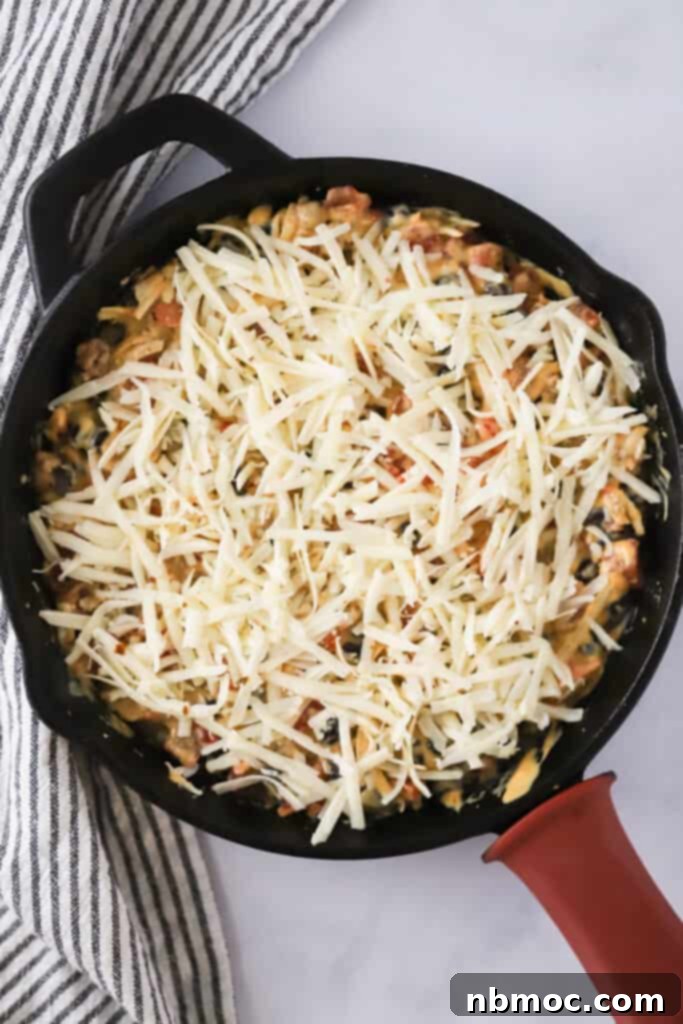 A cast iron skillet with queso topped with shredded cheese; loaded queso dip; cowboy queso, rotel queso.