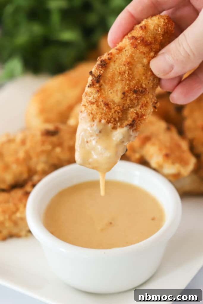 Crispy Golden Chicken Strips 2 A hand holding a homemade chicken tender and dipping in into sauce.