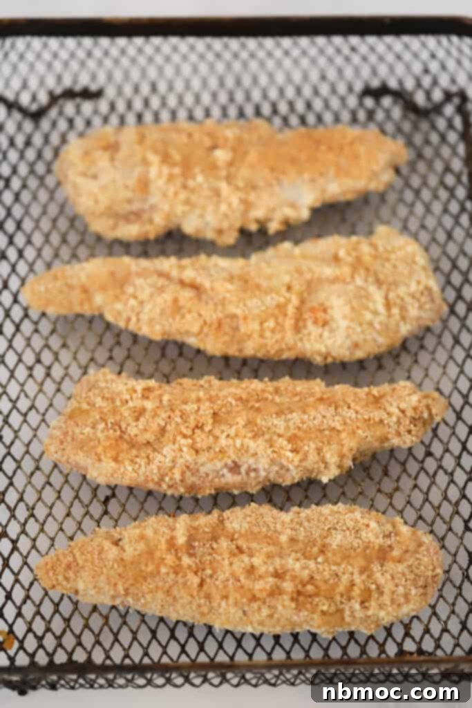 Breaded chicken tenders in an air fryer basket.