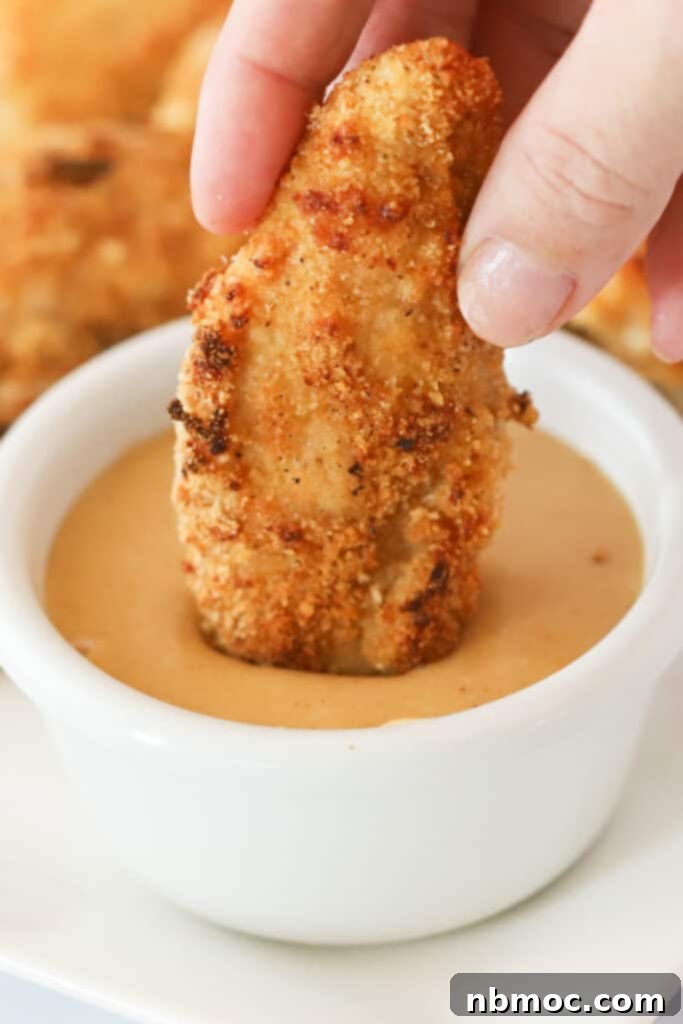 A hand dipping a chicken tender into a ramekin of sauce, best honey mustard sauce recipes. Honey mustard dip recipe.