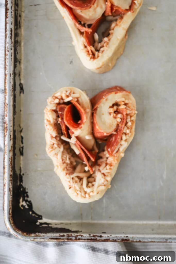 Cheesy Pizza Pinwheels 3 Pizza Roll Ups shaped into hearts on a sheet tray. pepperoni roll ups, pizza rolled up. Recipe for pizza roll ups. Pizza roll recipe.