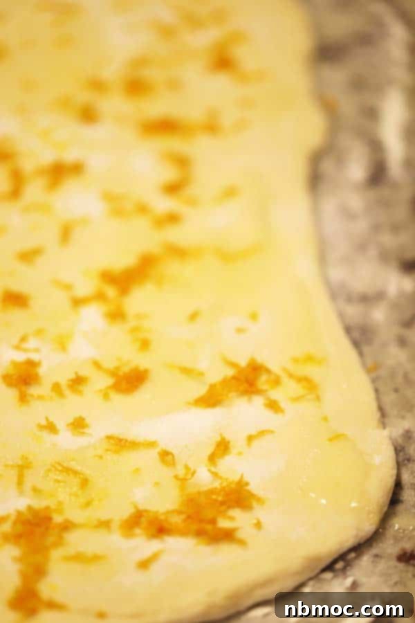 Rolling out orange sweet rolls dough on a clean countertop, preparing for the orange filling.