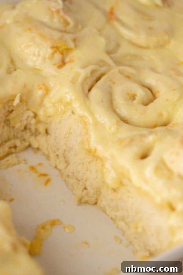 Close-up of baked orange sweet rolls, generously topped with creamy orange flavored frosting.