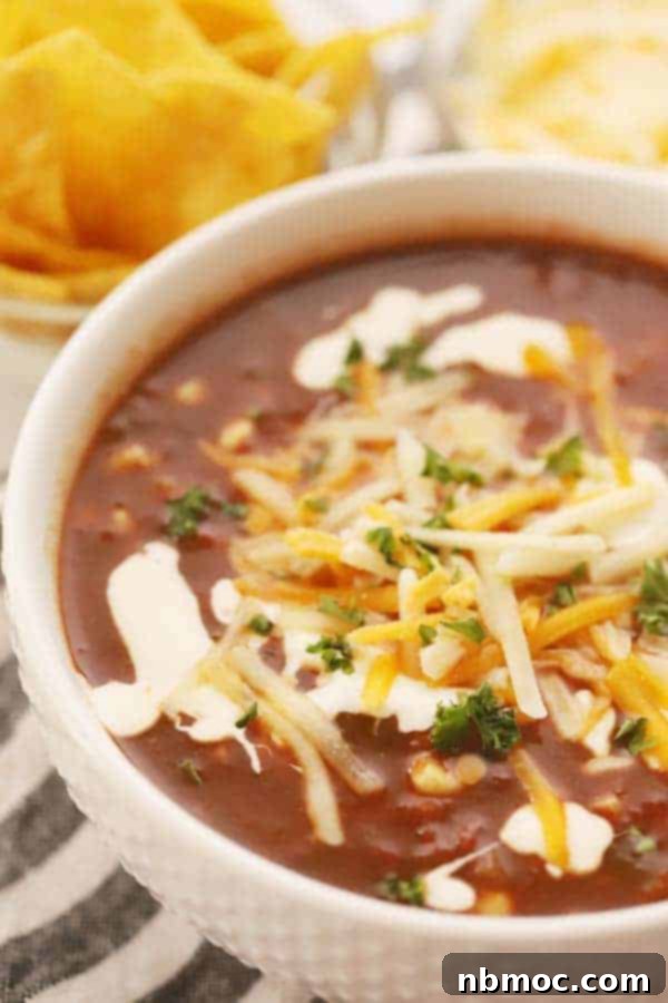 Zesty Black Bean Fiesta Soup 4 A beautiful white serving bowl showcasing vegetarian black bean soup with corn, elegantly topped with sour cream and shredded cheese for a hearty meal.