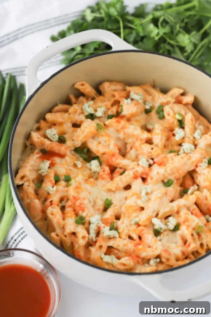 Fiery Buffalo Chicken Pasta 2 A Dutch oven filled with creamy Buffalo Chicken Pasta, garnished with fresh herbs and blue cheese, on a rustic wooden table.