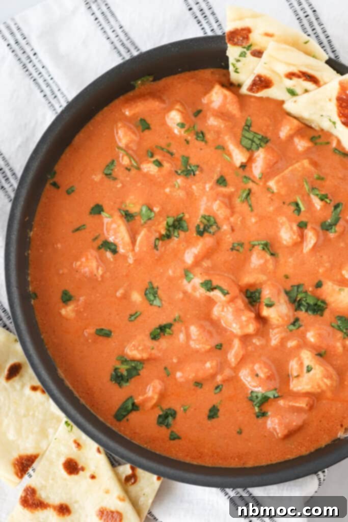 A bowl full of the best Chicken Tikka Masala topped with fresh cilantro and a side of Naan bread.