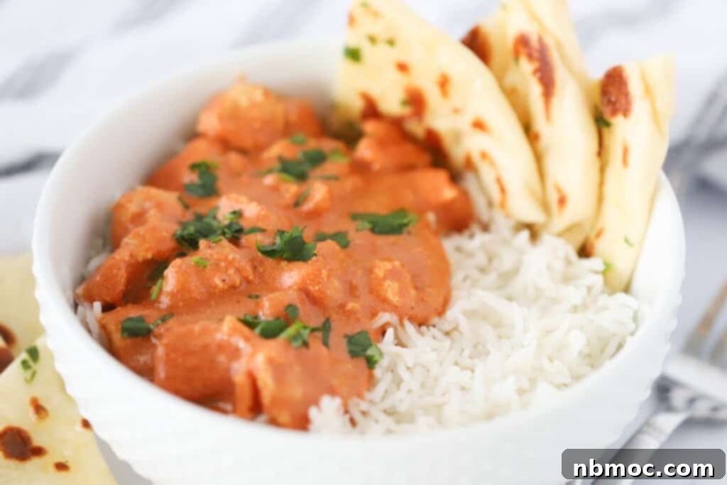 A white serving bowl full of Chicken Tikka Masala, rice, and Naan.