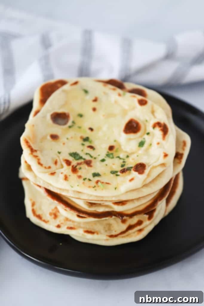 A stack of golden, soft homemade naan bread on a black plate, brushed with garlic butter. Perfect for any Indian meal.