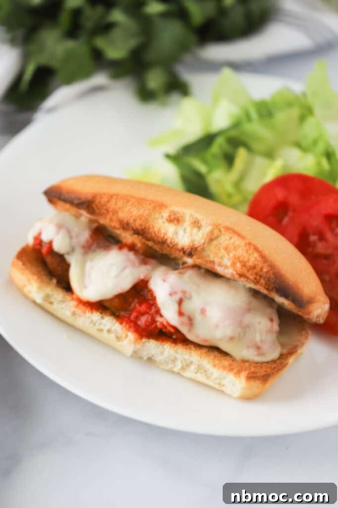 Saucy Meatball Hero 2 A dinner plate with a Meatball Marinara Sub Sandwich topped with melted cheese and marinara sauce; Meatball marinara sandwich recipe.