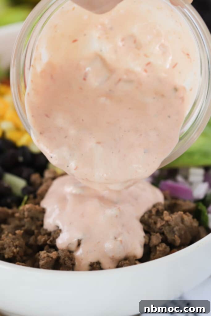 Taco Salad Dressing being poured over ground beef in a bowl.