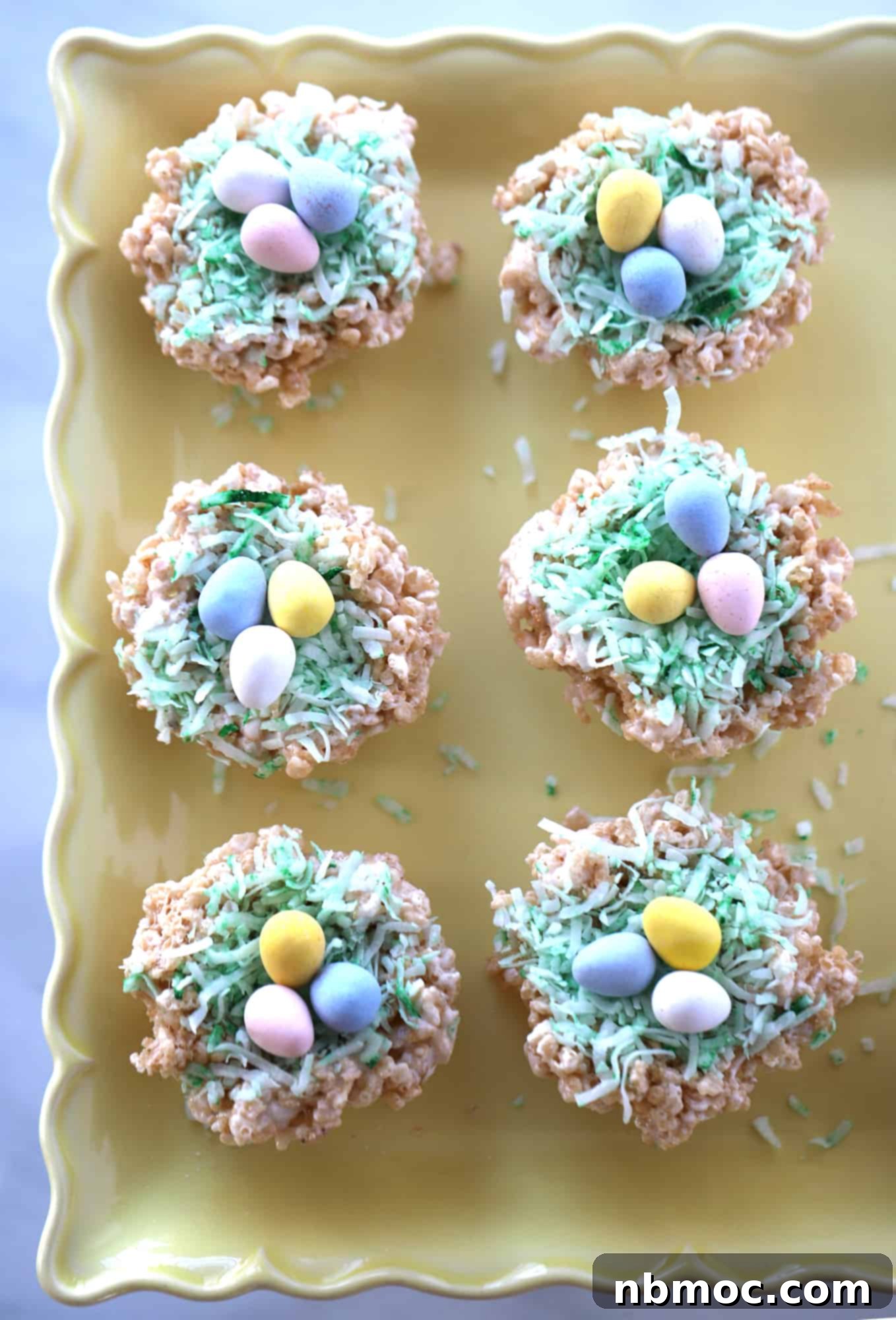 Adorable rice krispie easter nests on a serving plate, topped with coconut grass and egg candies.