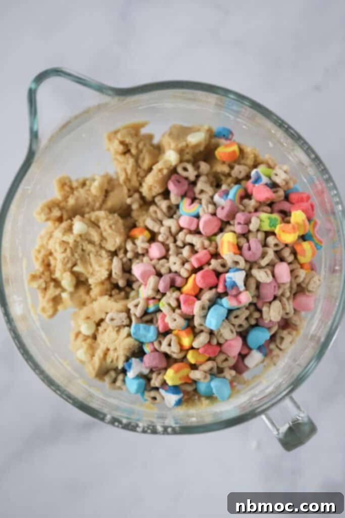 A measuring cup filled with colorful Lucky Charms marshmallows and white chocolate chips, alongside other cookie ingredients, showcasing the preparations for making these magical cookies.