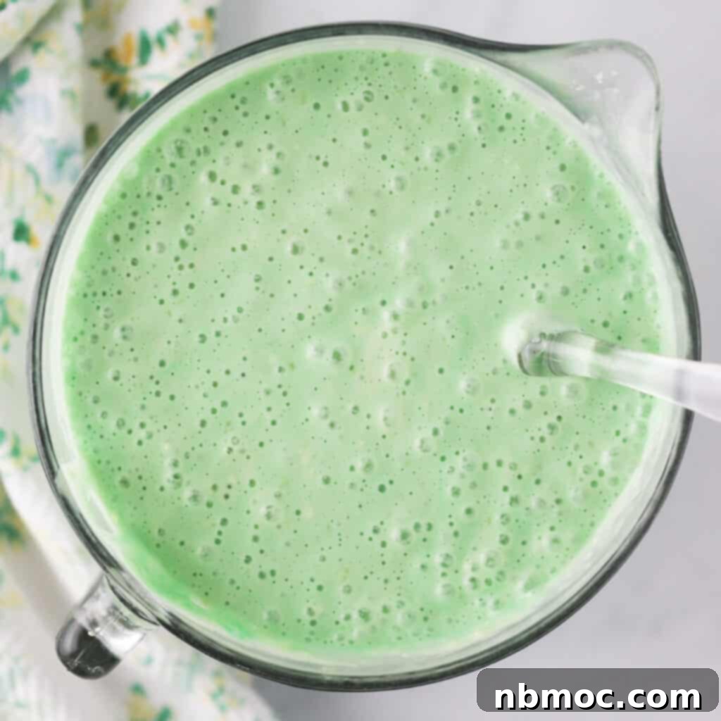 Measuring cup filled with vibrant green batter, ready to create delightful shamrock pancakes for St. Patrick's Day. This is the perfect green pancake mix for an Irish green breakfast.