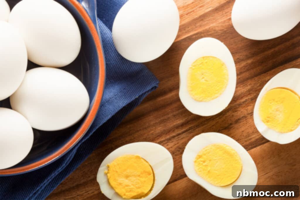 A bowl of hard boiled eggs next to cooked eggs cut in half, highlighting the perfect texture achieved with baking soda. Learn how to get easy peel, perfectly cooked hard boiled eggs.