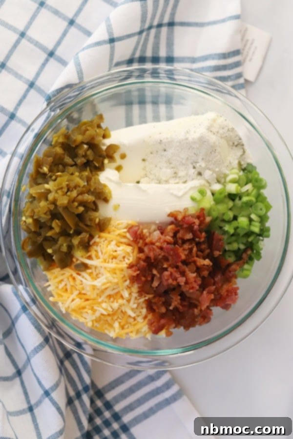 Kickin' Jalapeño Cheese Ball 4 All the vibrant ingredients for the Jalapeno Popper Cheese Ball, including cream cheese, bacon, shredded cheddar, green onions, and canned jalapeños, neatly arranged in a glass mixing bowl on a countertop.