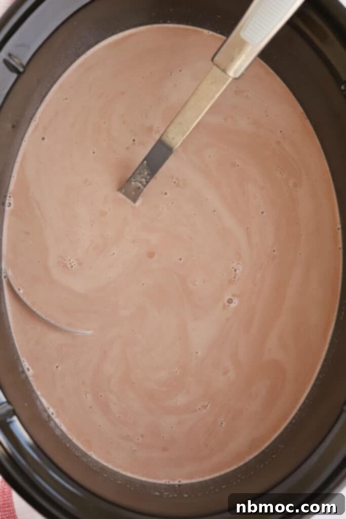 A large crockpot filled with steaming hot chocolate, ready to be served. Made with condensed milk and cocoa powder, it promises a rich and creamy texture.