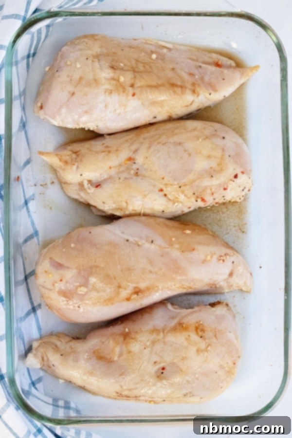 Baked Lemon Ginger Chicken breast, chicken lemon ginger marinated. Raw chicken breasts marinating in a glass bowl with lemon and ginger slices.