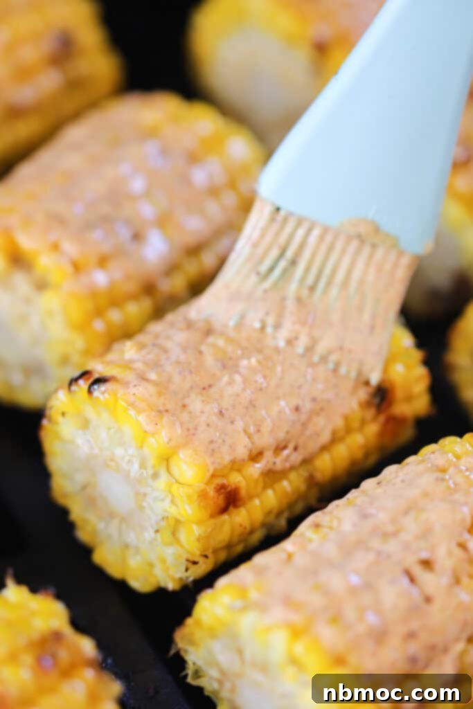 Brushing crema over the tops of grilled mexican street corn.