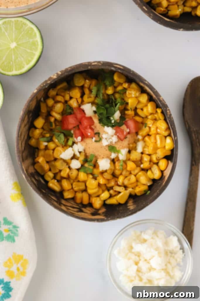 A bowl of mexican street corn off the cob topped with sauce, cheese, tomatoes, and fresh cilantro.