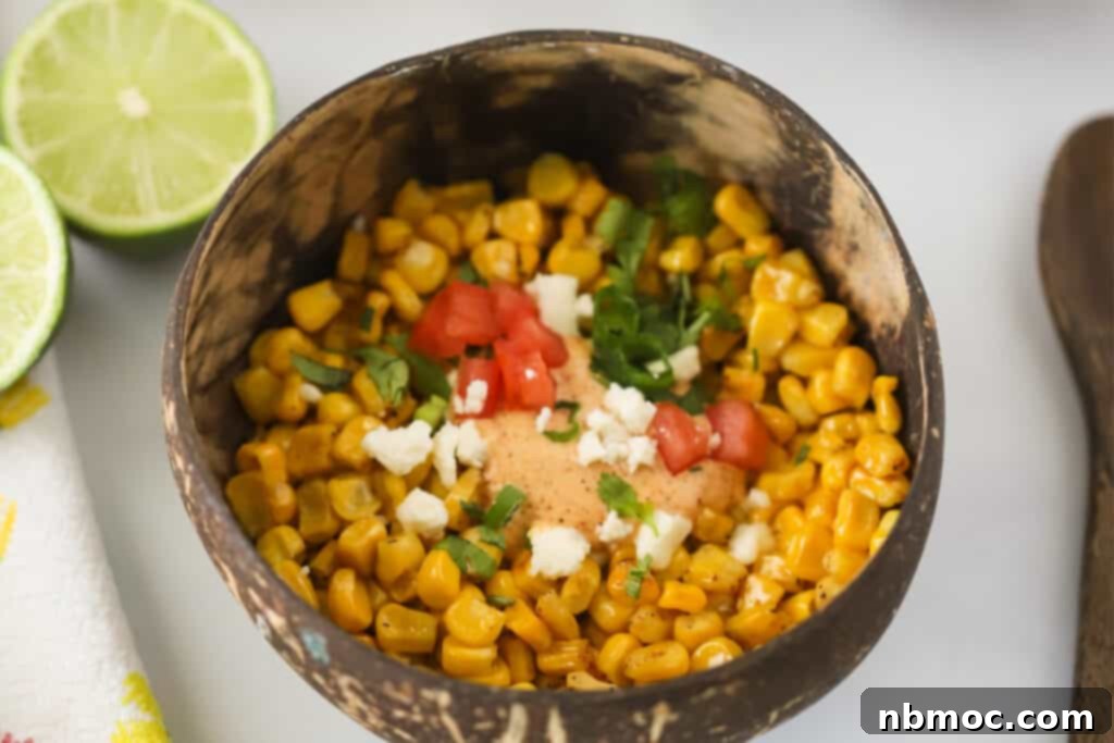 Mexican corn side dish in a small bowl with toppings and a fresh lime.
