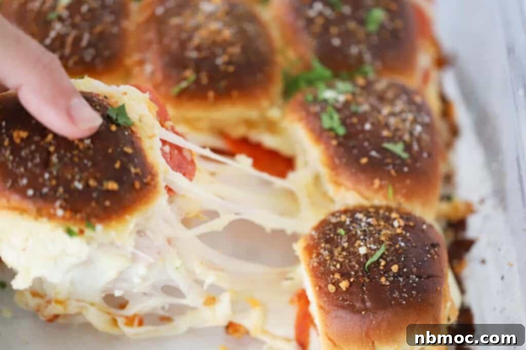 A hand reaching for a warm, cheesy pizza slider from a baking tray, highlighting the irresistible melty cheese and toppings.