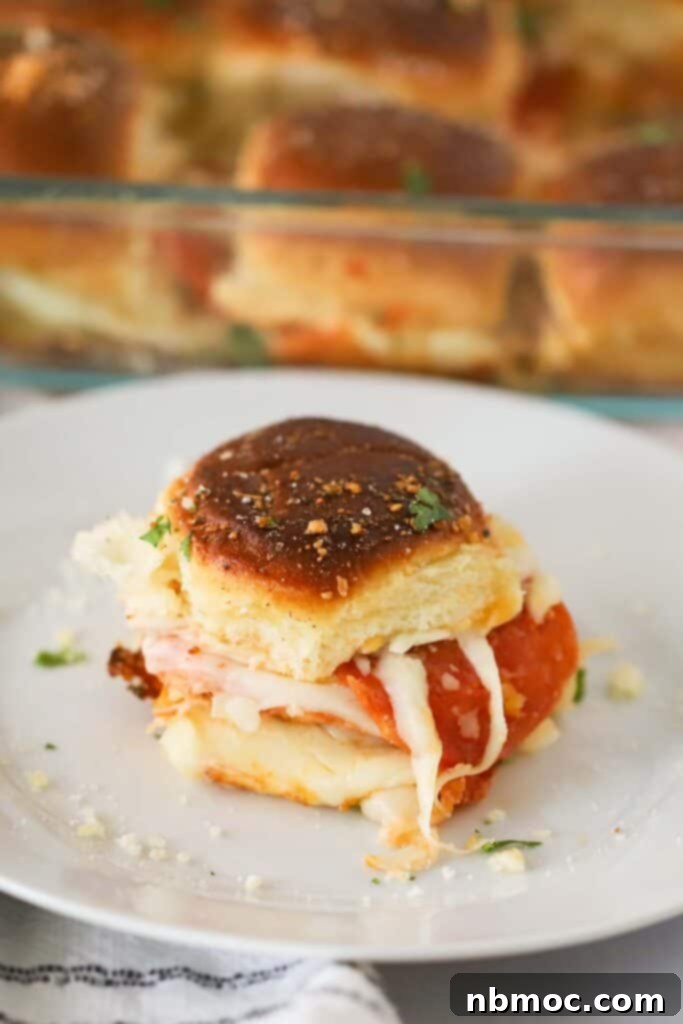 A close-up of a single pepperoni pizza slider on a plate, showing the melted cheese, golden crust, and vibrant pepperoni filling.