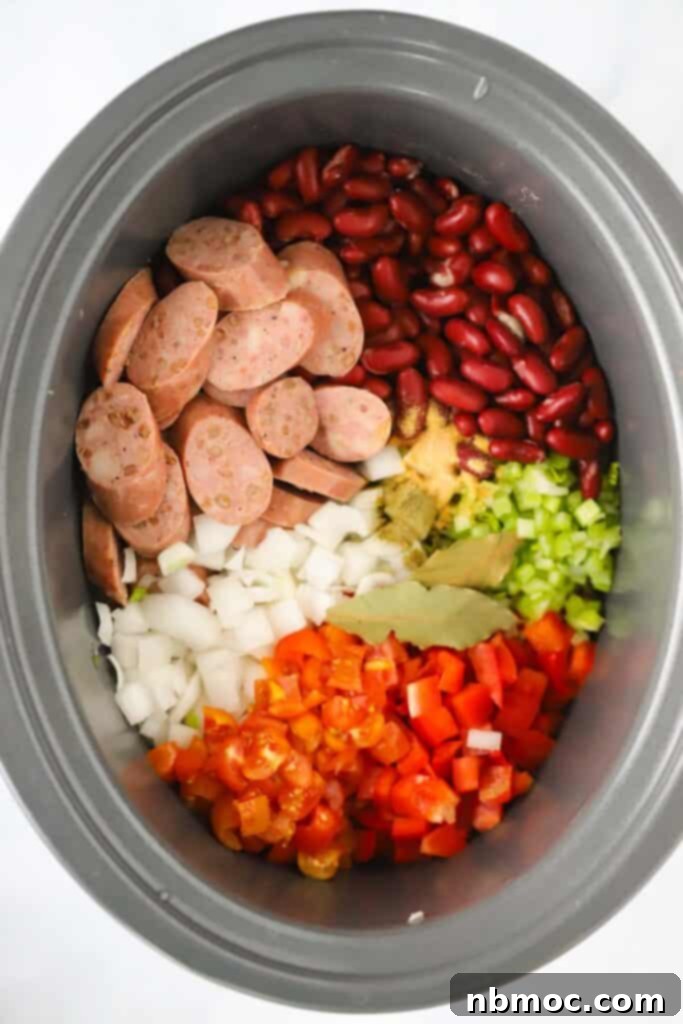 A crockpot full of ingredients to make slow cooker rice and beans with sausage.