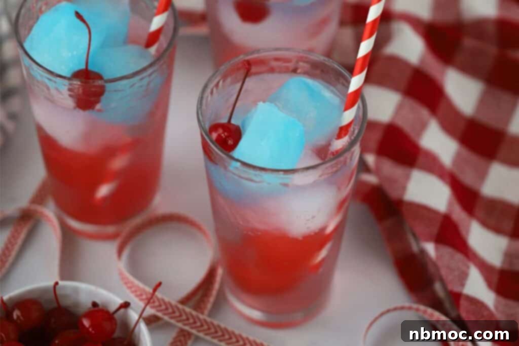 Two glasses with red white and blue 4th of july drinks made with colorful ice cubes of gatorade and maraschino cherries.