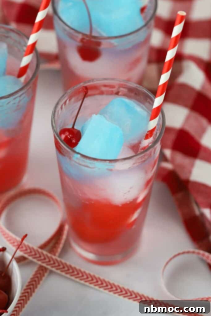 A tall glass full of Sprite with red white and blue gatorade ice cubes and a colorful straw.