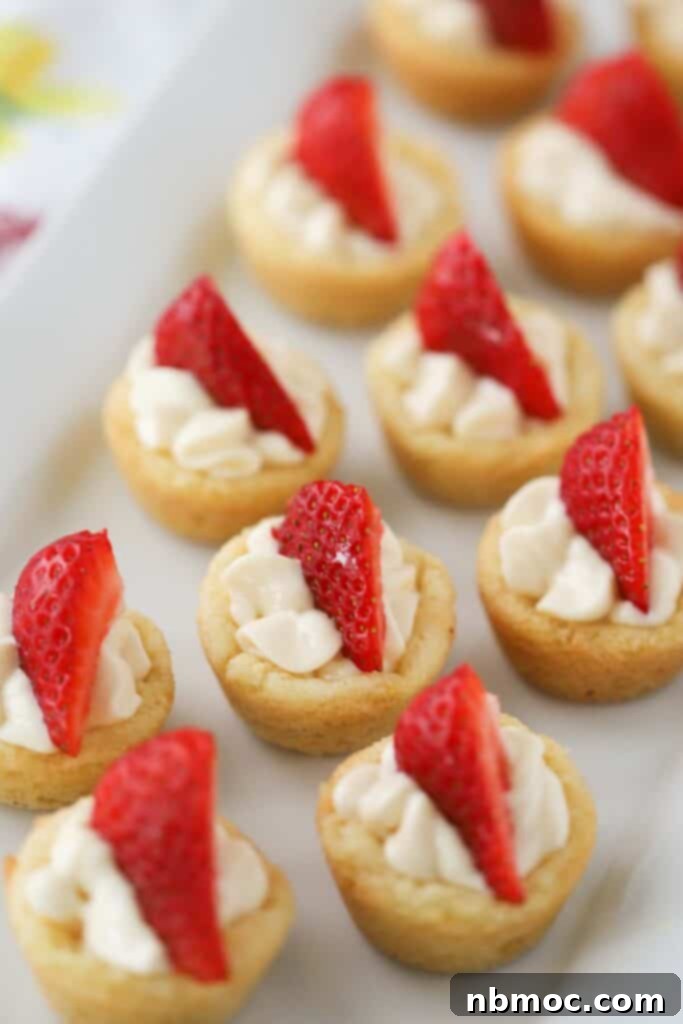 Rows of mini lemon cookies topped with whipped cream and fresh strawberries.