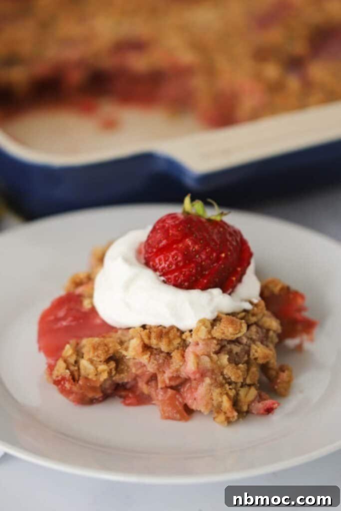 Sweet and Tangy Strawberry Rhubarb Crisp 2 A plate with a serving of this strawberry rhubarb crisp recipe topped with whipped cream and a fresh strawberry.