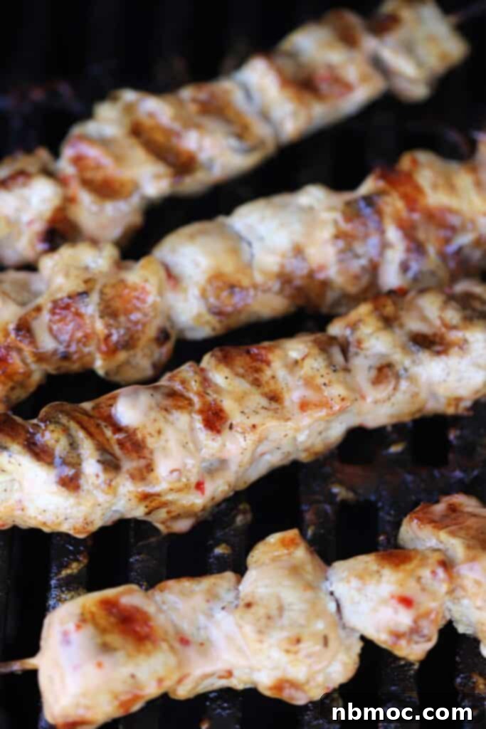 Bang bang chicken skewers cooking on a grill, showing the golden-brown char and rich sauce.