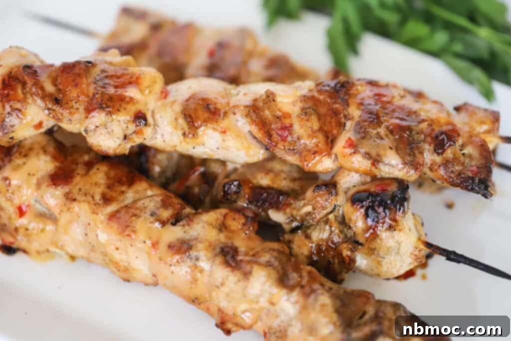 A beautifully arranged platter of grilled bang bang chicken skewers, garnished with sesame seeds.