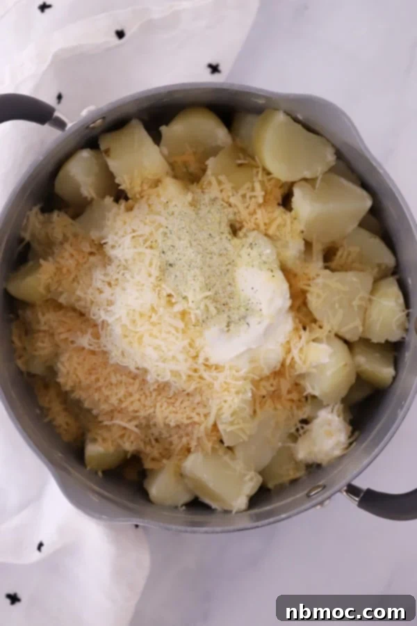 A pot filled with mashed potatoes, alongside bowls of shredded Gruyere and Parmesan cheese, sour cream, and butter, ready for mixing.