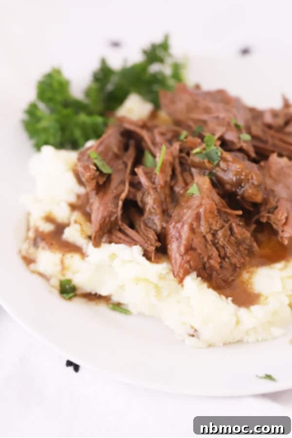 A close-up shot of a plate of creamy Gruyere mashed potatoes, garnished with a sprig of fresh rosemary and topped with tender short rib.