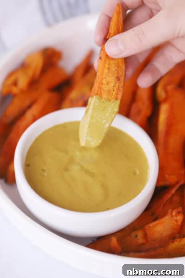 Crispy Sweet Potato Fries with Zesty Dipping Sauce 4 Hand dipping crispy baked sweet potato fries into a ramekin of homemade chipotle lime mayo.