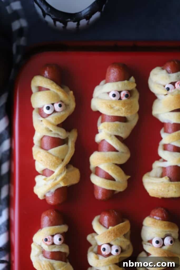 A tray with mummy hot dogs, decorated using crescent roll dough and candy eyes. Perfect for Halloween parties.
