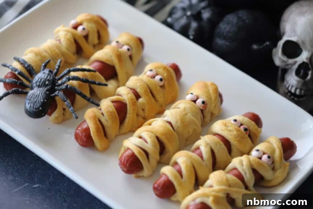 Mummy hot dogs on a plate ready to eat, garnished with candy eyes.