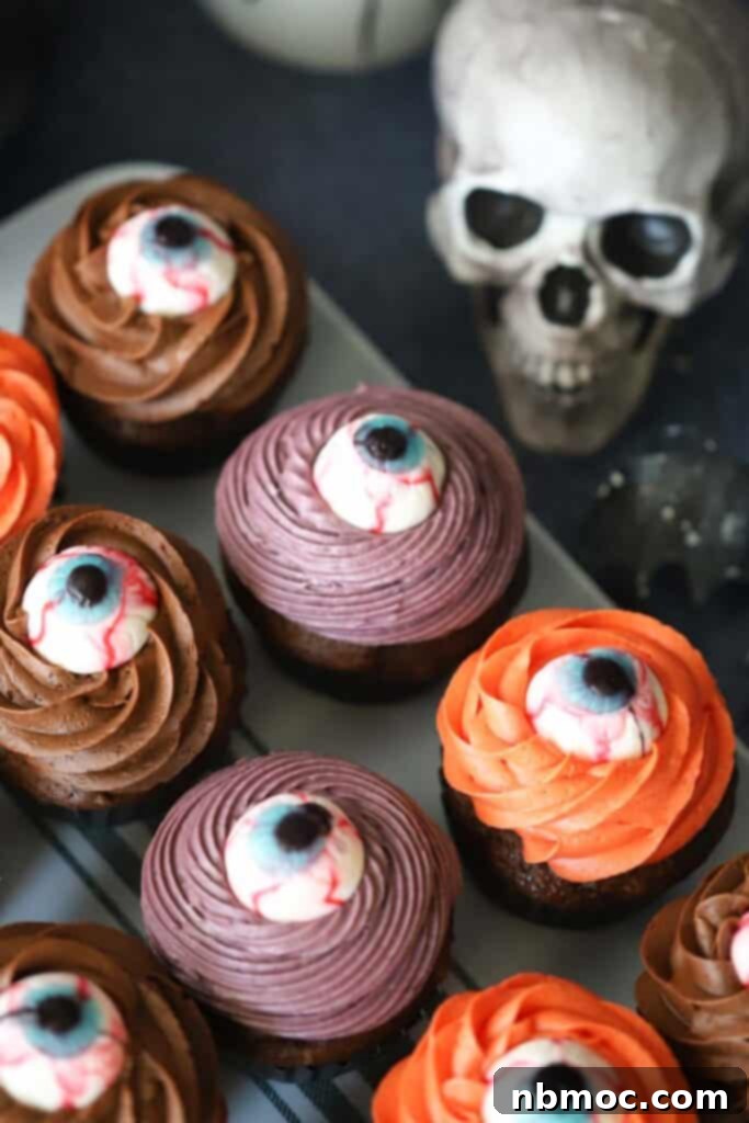 A tray full of Halloween themed cupcakes topped with colored frosting and candy eyeballs.