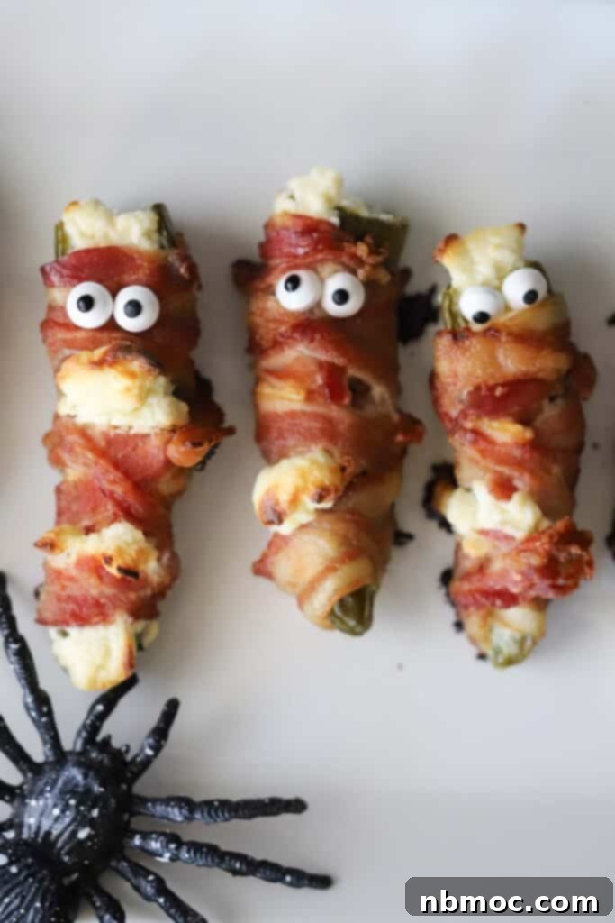 A row of mummy jalapeno poppers wrapped with bacon, ready to serve for Halloween.