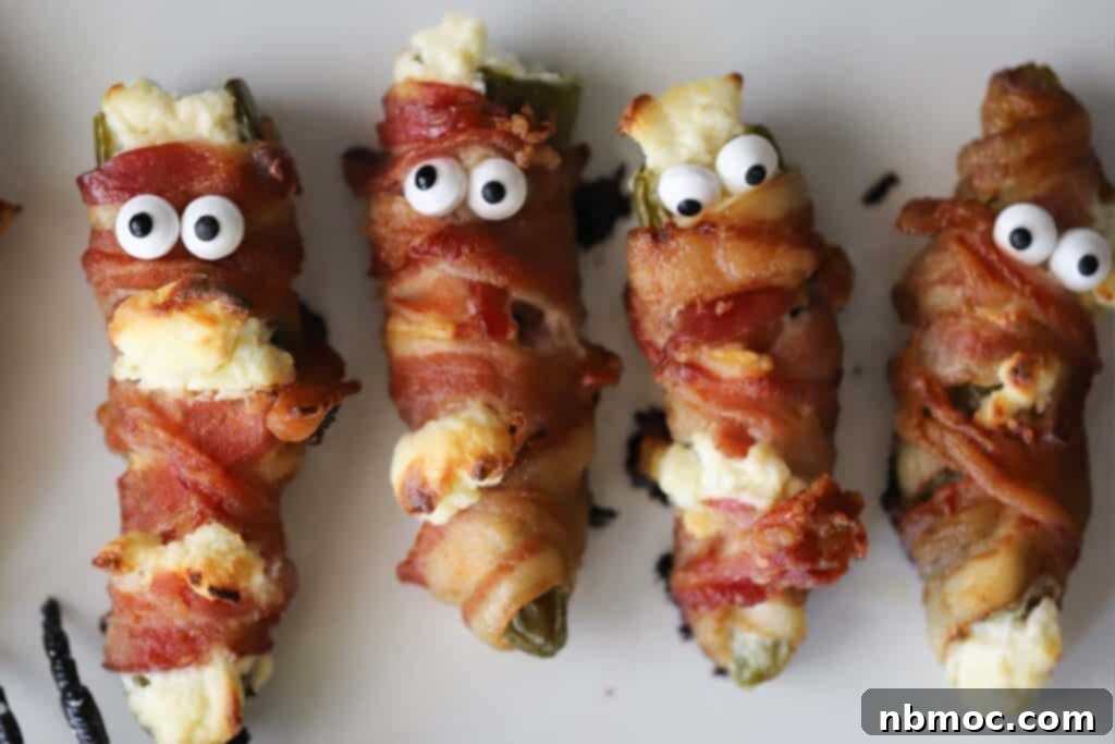 Halloween mummy jalapeno poppers adorned with candy eyes and wrapped in crispy bacon.