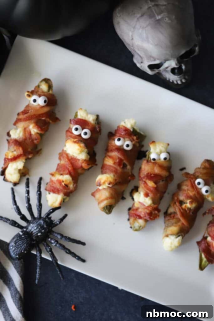A serving plate filled with a row of festive Halloween mummy jalapeno poppers, ready for guests.