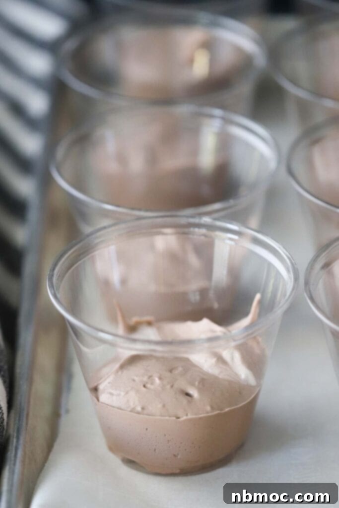 Haunted Earth Pudding Cups 4 chocolate pudding in the bottom of plastic cups, showing the initial layering step for graveyard dirt cups.