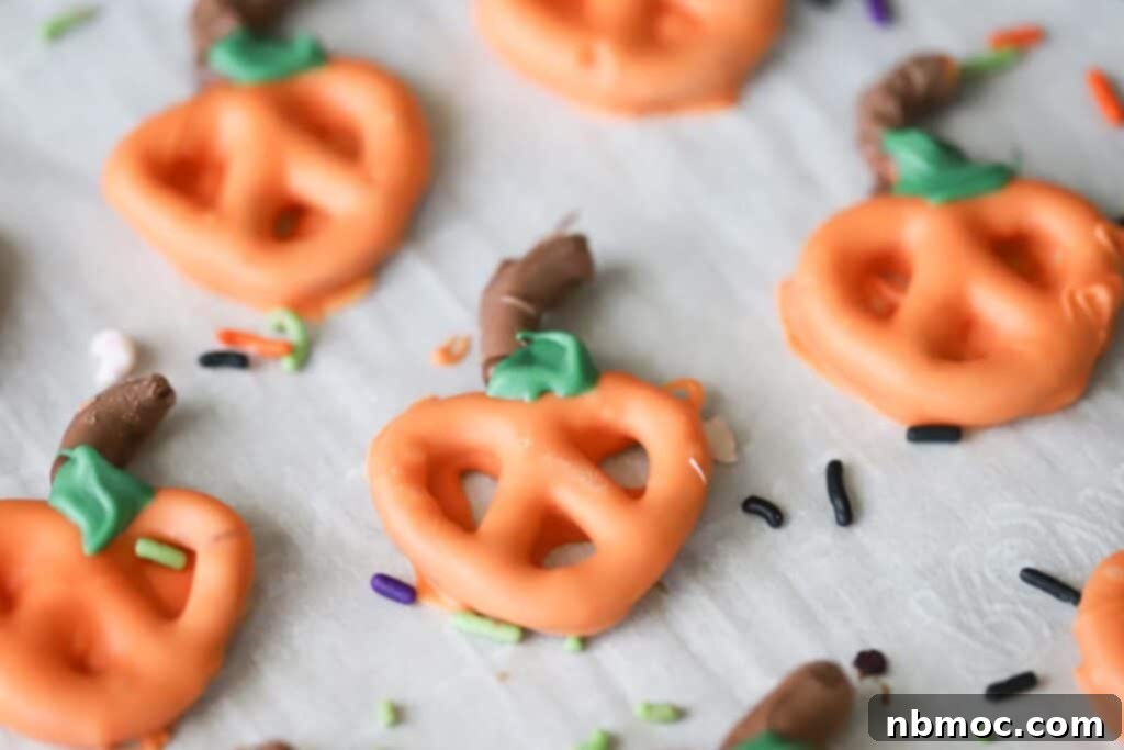 Spiced Pumpkin Pretzel Twists 5 A cluster of beautifully decorated Halloween pumpkin pretzels on a rustic wooden board, showcasing their vibrant orange chocolate, milk chocolate stems, and green leaves.