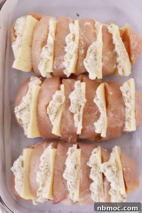 Accordion Style Green Chile Chicken 4 hasselback green chili chicken breast stuffed with a green chile and cream cheese filling, uncooked in a glass baking dish.