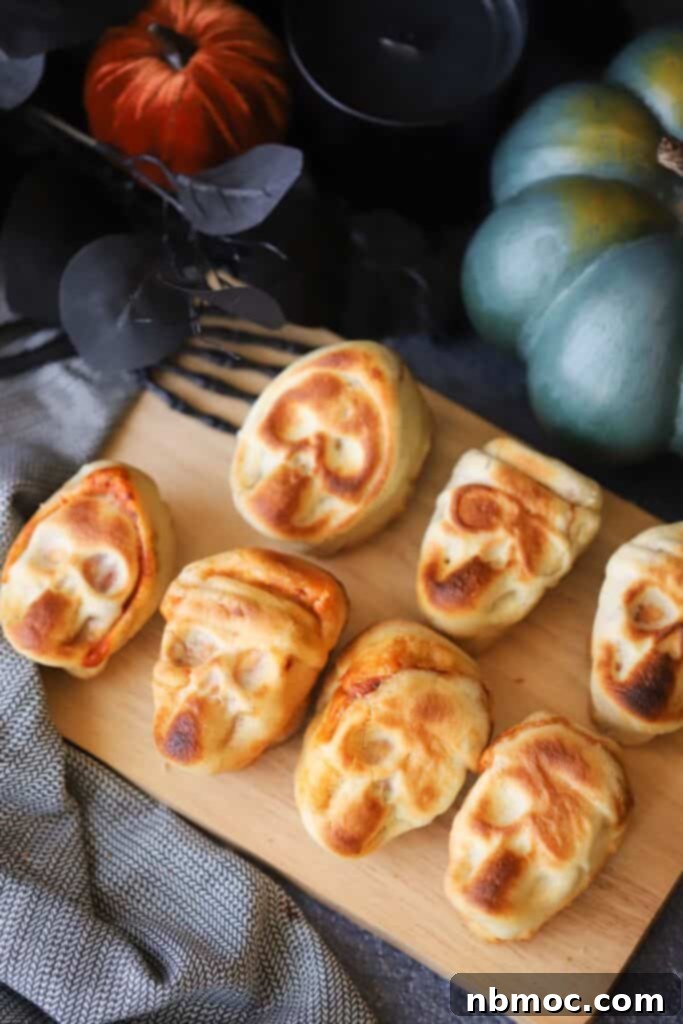 Halloween Pizza Skulls on a cutting board, the perfect pizza pockets for halloween parties. These individual skull-shaped pizzas are filled with cheese and pepperoni, ready for a spooky snack.