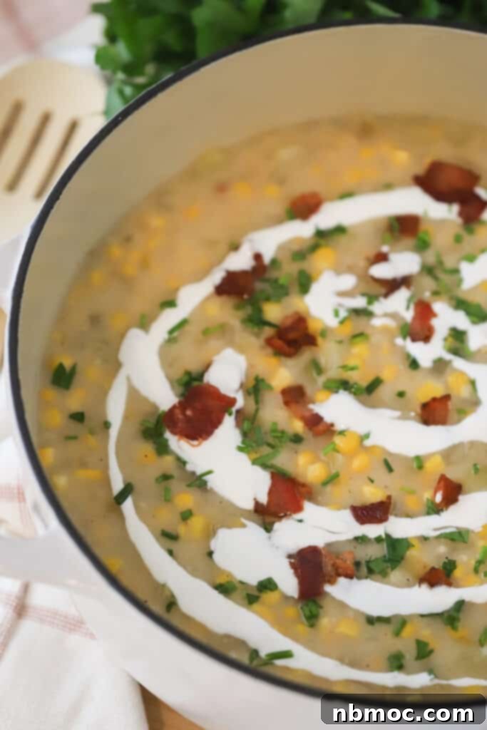 Golden Harvest Chowder 4 A close-up shot of a large Dutch oven filled with rich, creamy potato corn chowder. The soup is beautifully garnished with a swirl of creme fraiche, an abundance of crispy bacon bits, and vibrant fresh parsley, creating an inviting and hearty meal. This image highlights the delicious appeal of an easy potato chowder soup, ready to be enjoyed.