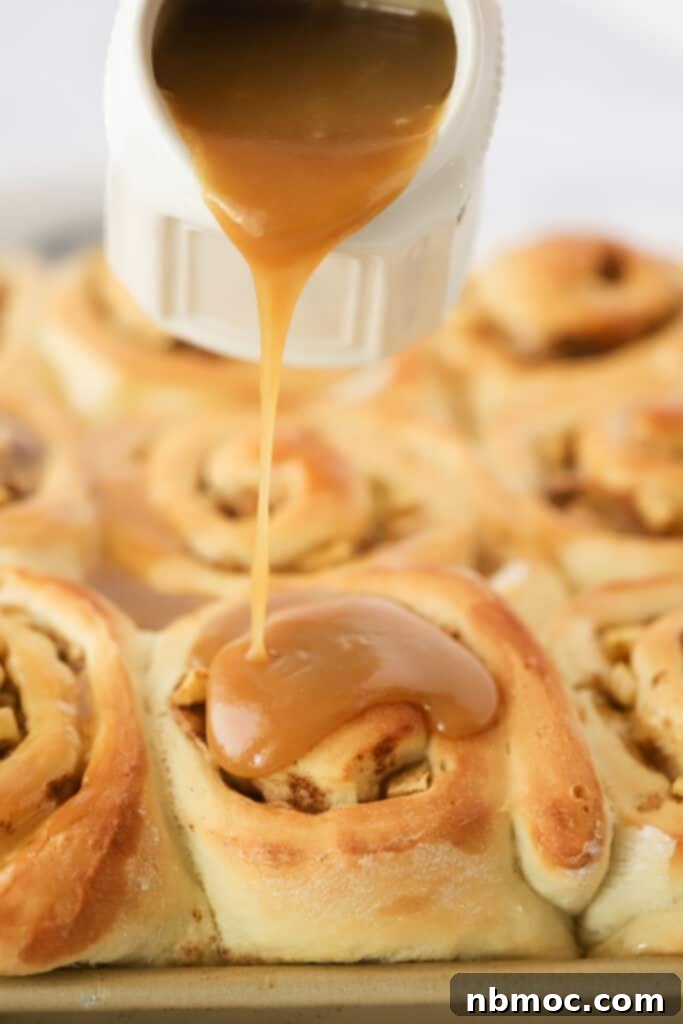 Rich, homemade caramel sauce being poured generously over warm apple caramel cinnamon rolls.